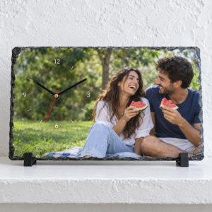 שעון אבן בזלת 30×20 – זוג בפיקניק על מעמדים שחורים לפני קיר לבן מחוספס